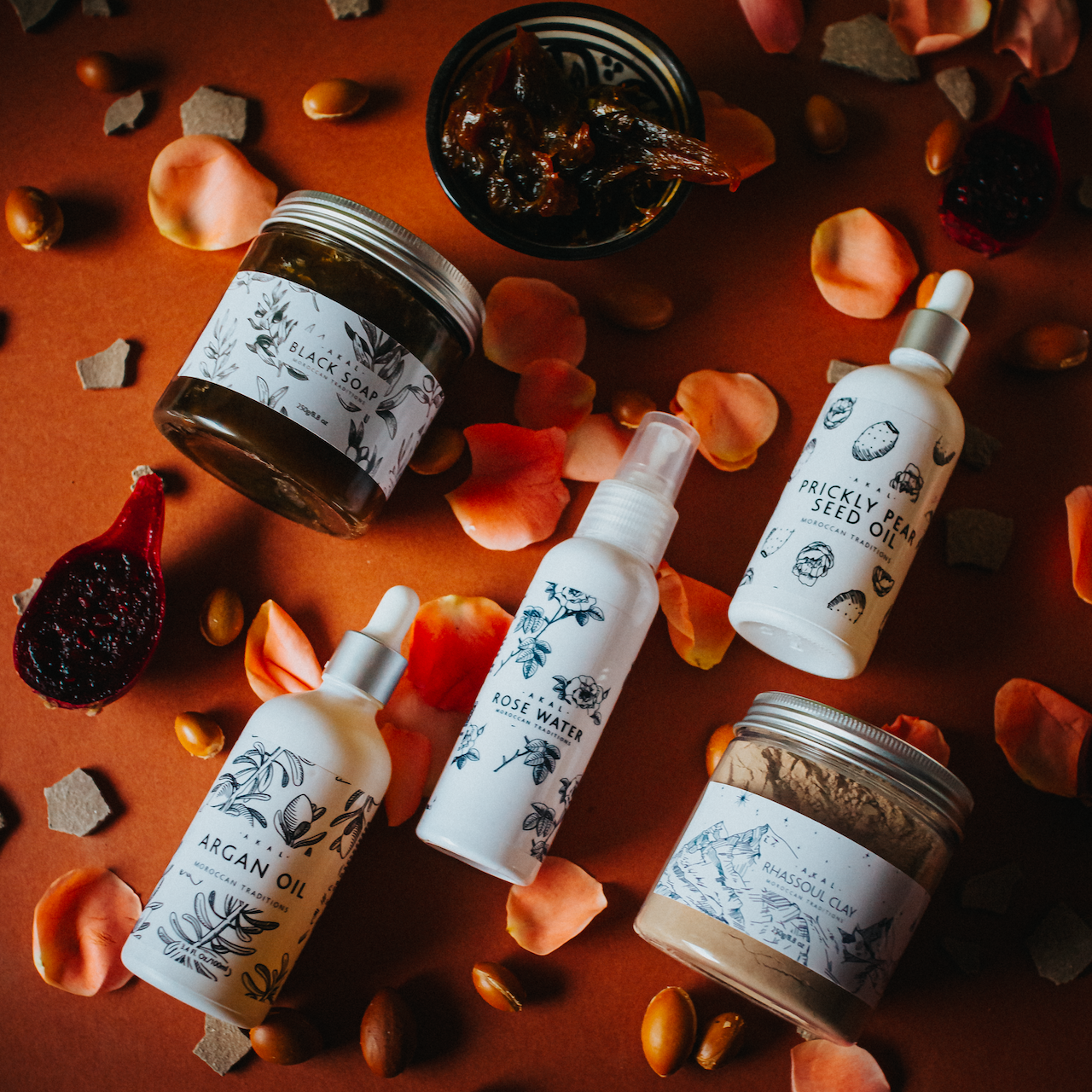 Picture of all the products, layed down on a burnt orange background with fruits and petals around